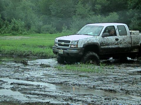 1987 Suzuki Samurai - Pickup truck is stuck in a muddy field with trees in the background.