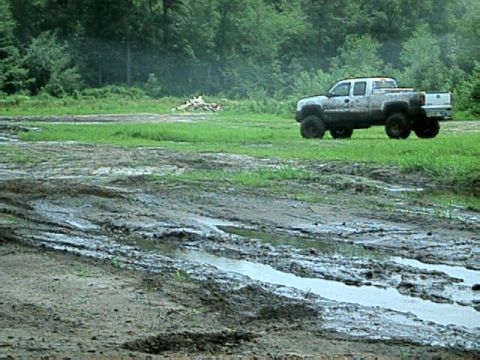1987 Suzuki Samurai - A white pickup truck navigates a muddy terrain with trees in the background.