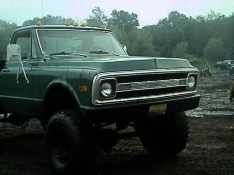 1987 Suzuki Samurai - This lifted green pickup truck features a prominent chrome grille and appears to be from the early 1970s, not a 1987 Suzuki Samurai.
