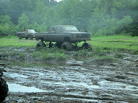 1987 Suzuki Samurai - Two pickup trucks navigate a muddy off-road course.
