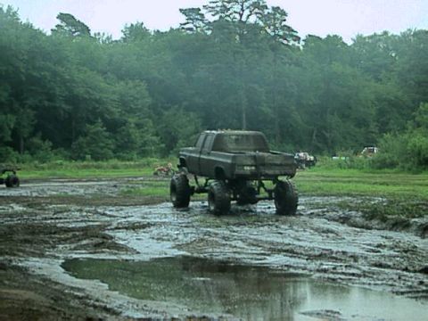 1987 Suzuki Samurai - A lifted pickup truck navigates a muddy terrain with other vehicles visible in the distance.