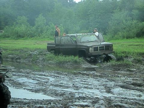 1987 Suzuki Samurai - Off-road truck attempts to navigate a muddy terrain, with onlookers present.
