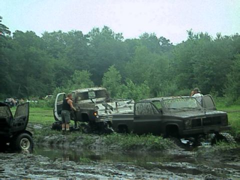 1987 Suzuki Samurai - Two pickup trucks are stuck in a muddy field, with people standing near them.