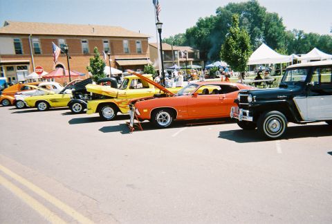 1972 Ford Ranchero - Several vehicles are parked in a line at an outdoor event, including an orange muscle car and a yellow pickup truck.