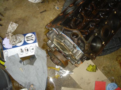 1986 Ford Mustang - Engine block and associated parts are disassembled on a garage floor, suggesting a repair or modification process.