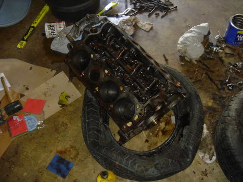 1986 Ford Mustang - An engine block sits on a tire in a garage, surrounded by tools and debris, suggesting a repair or rebuild in progress.