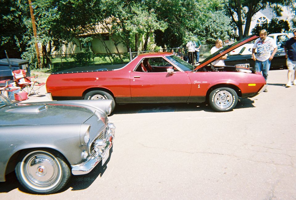 Red 1970s Ford Ranchero 500 with hood open at a car show, silver Thunderbird in foreground