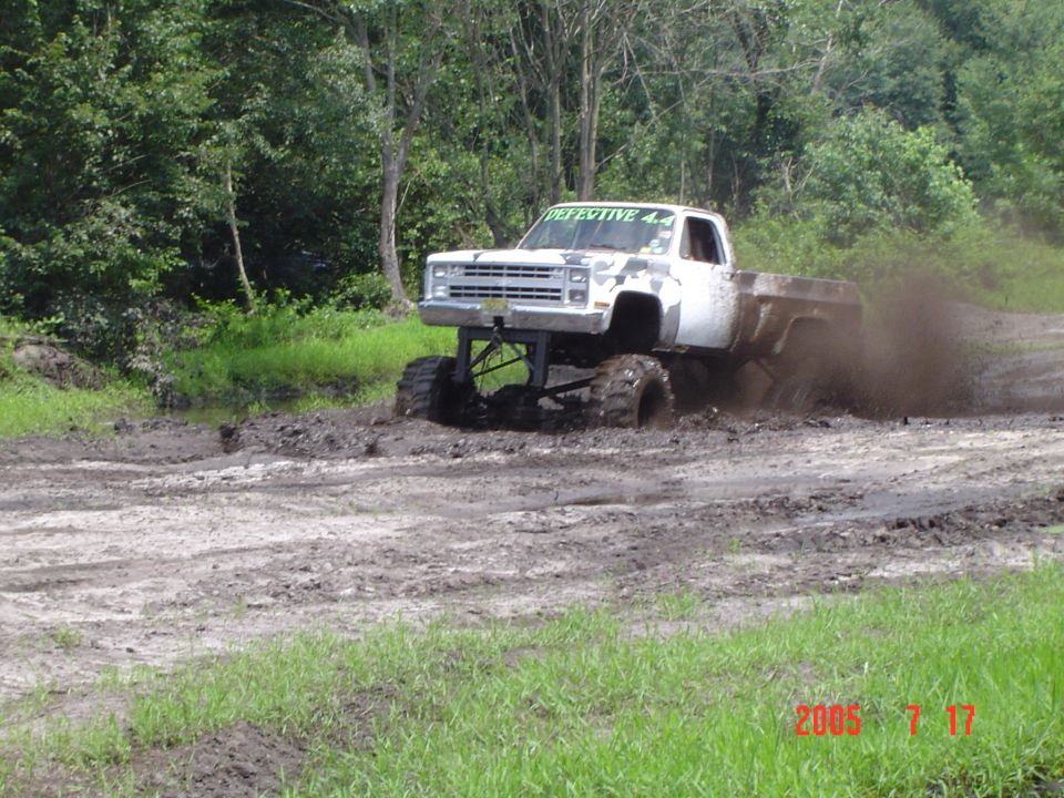 Lifted white square-body Chevy pickup slinging mud through a mud bog