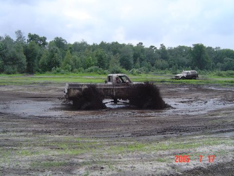 1995 Dodge 1500 - A pickup truck churns mud as it drives through a field, with another vehicle in the distance.