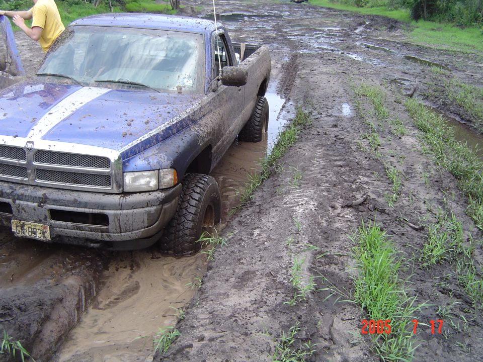 1995 Dodge 1500 pickup truck with blue and white stripes stuck in mud on a dirt track