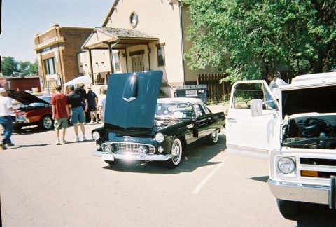1972 Ford Ranchero - Two classic cars are parked on a street with their hoods open, attended by onlookers.