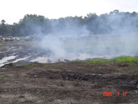 1995 Dodge 1500 - Mud bog event with several trucks and spectators visible in the distance under a smoky sky.