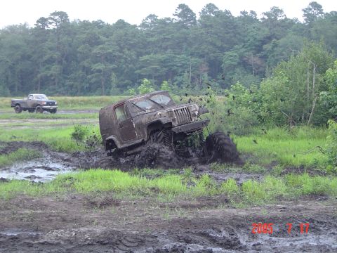 1995 Dodge 1500 - A Jeep Wrangler is deeply stuck in a mud pit, with another truck visible in the distance.