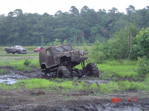1995 Dodge 1500 - Modified Jeep Wrangler is stuck in a muddy field with two trucks in the distance.