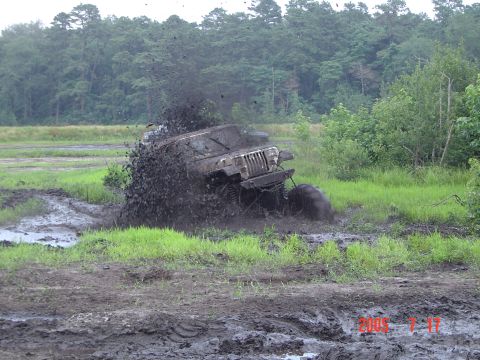 1995 Dodge 1500 - A Jeep Wrangler TJ navigates a muddy obstacle course, kicking up a large spray of mud.