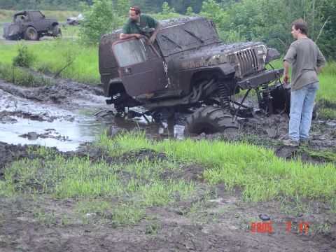 1995 Dodge 1500 - Two men observe a heavily mud-caked Jeep Wrangler submerged in a muddy field.