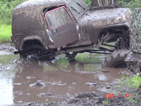 1995 Dodge 1500 - This heavily modified off-road vehicle is deeply stuck in mud, with its door open and suspension and exhaust visible.