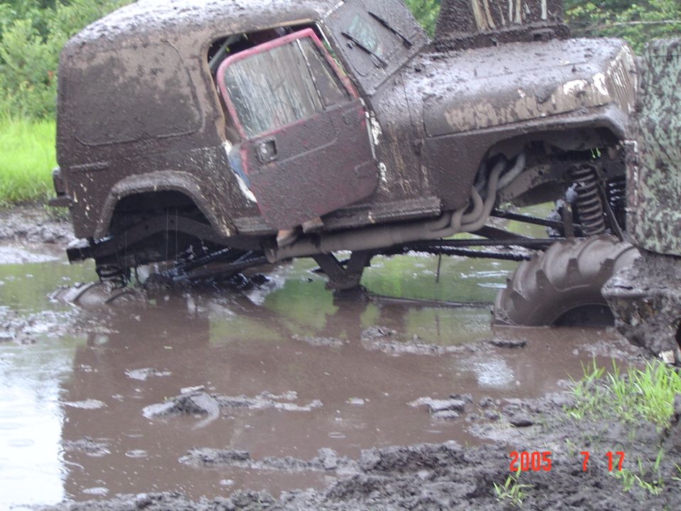 Mud-covered off-road vehicle stuck in mud with open door and exposed engine components