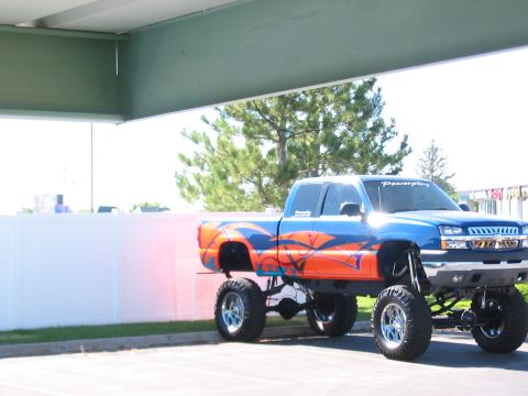 1991 Ford Bronco - A custom-painted, lifted pickup truck is parked under an overhang.