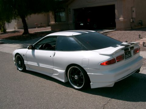 1996 Ford Probe - A white 1996 Ford Probe with black racing stripes is parked in front of a house.