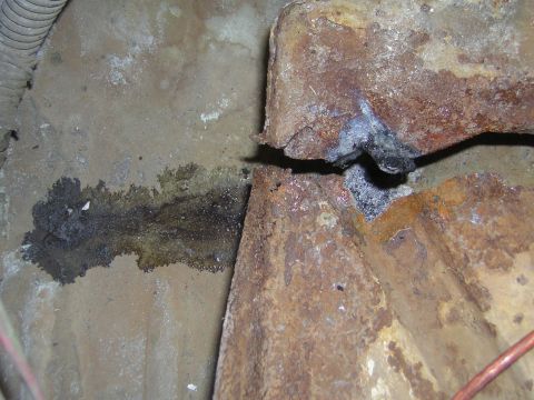 1995 Ford Bronco - Close-up view of heavily rusted metal components with a dark fluid stain on the surrounding surface.