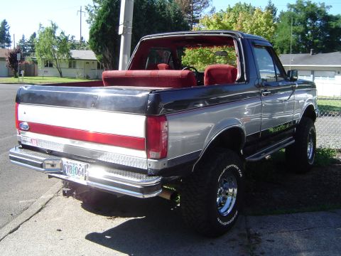 1989 Ford Bronco - Rear 3/4 view of a lifted 1989 Ford Bronco with a two-tone paint scheme and red interior.