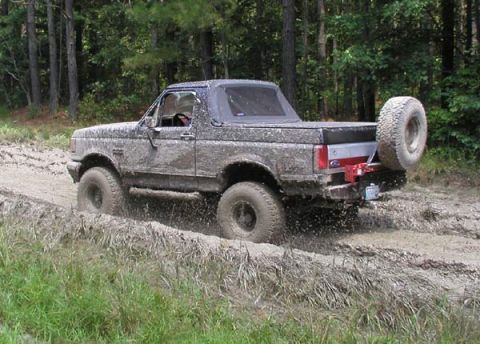 1988 Ford Bronco - 1988 Ford Bronco navigating a muddy off-road path, kicking up dirt and water.