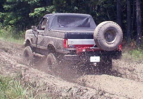 1988 Ford Bronco - This SUV is navigating a muddy trail, kicking up dirt and water as it goes.