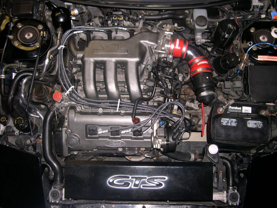 Engine bay with V6 engine, red intake hose, and Duracell battery. GTS logo visible