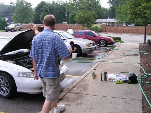 1993 Ford Taurus - People washing a white 1993 Ford Taurus and a silver sedan in a parking lot.