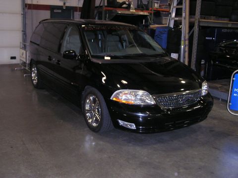 1993 Ford Taurus - This black minivan is parked inside a garage or workshop with shelving in the background.