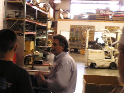 1993 Ford Taurus - A group of people are gathered in a warehouse, with shelves stocked with parts and a forklift in the background.