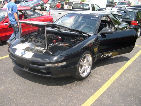 1997 Ford Probe - Black Ford Probe GTS coupe at an outdoor car show with the hood and driver's door open, revealing a turbocharged V6 with a red-anodized tur…