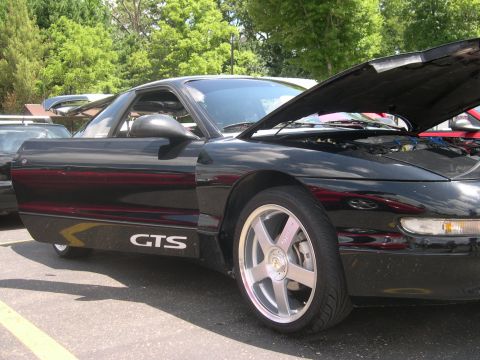 1997 Ford Probe - Low side view of a black hatchback coupe parked on asphalt at an outdoor car show with its hood propped open. White 'GTS' lettering sits on…