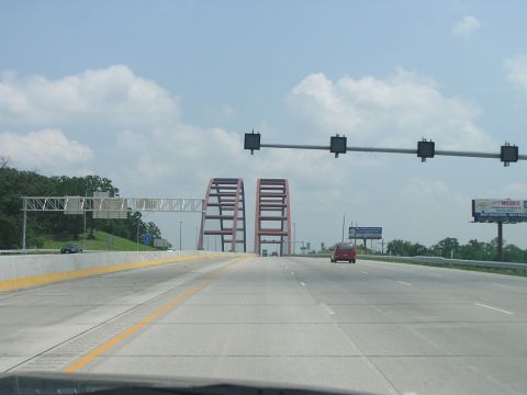 1993 Ford Taurus - A red car travels down a highway, approaching a distinctive bridge structure under a partly cloudy sky.