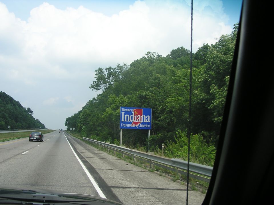 Indiana welcome sign on highway with trees and a car driving away