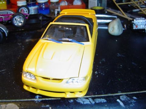1979 Ford Bronco - A yellow model car sits on a workbench surrounded by various hobby supplies and tools.