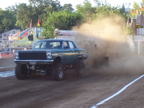 1994 Ford F-150 - A monster truck competes in a pulling event, kicking up a large cloud of dust.