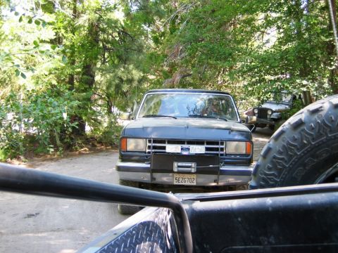 1985 Ford Bronco - A dark blue 1985 Ford Bronco is parked on a dirt road, with a winch mounted on the front bumper and a license plate visible.