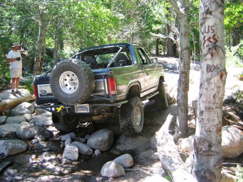 1985 Ford Bronco - A 1985 Ford Bronco navigates a challenging off-road course with large rocks and trees.