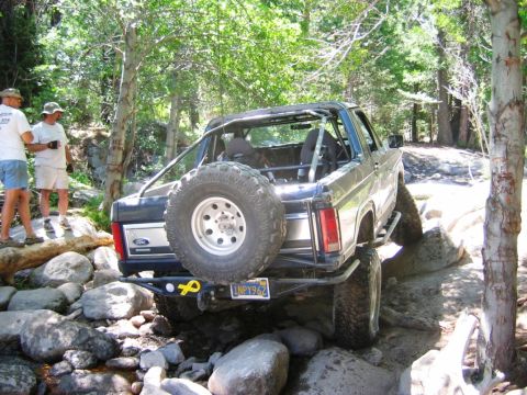 1985 Ford Bronco - A Ford Bronco navigates a challenging rocky terrain with two onlookers observing.
