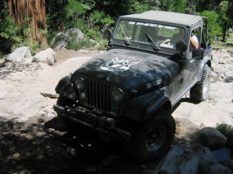 1985 Ford Bronco - Jeep CJ-7 navigating a rocky trail with a deer decal on its hood.