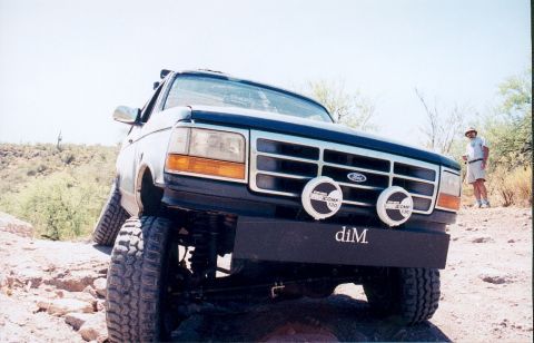 1994 Ford Bronco - A man stands near a lifted Ford Bronco on a rocky, desert-like trail.