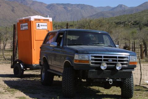 1994 Ford Bronco - A dark green 1994 Ford Bronco is seen towing a portable toilet in a dry, mountainous landscape.