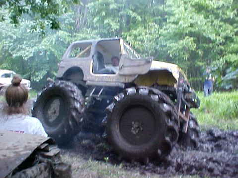 1987 Suzuki Samurai - A heavily modified vehicle with oversized tires navigates a muddy terrain, with another vehicle visible in the background.