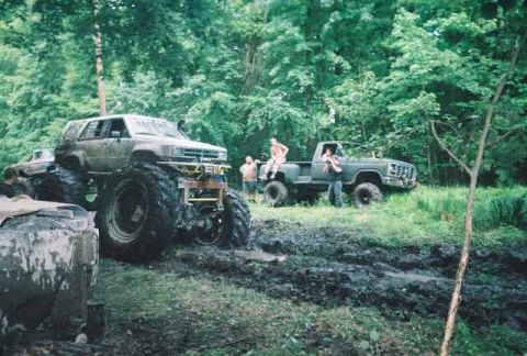 1987 Suzuki Samurai - Two modified trucks are stuck in the mud during an off-road event.