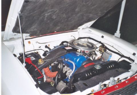 1978 Ford Mustang II - The engine compartment of a white vehicle is shown with the hood open, revealing the motor and various components.