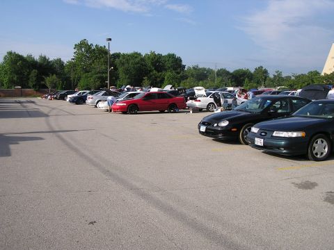 1993 Ford Taurus - A variety of cars are parked in an outdoor lot on a sunny day, with trees and buildings in the background.