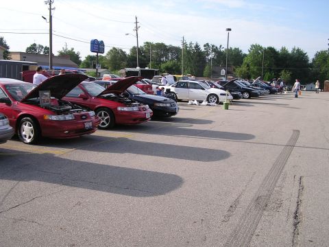 1993 Ford Taurus - Several cars are lined up in a parking lot with their hoods open.