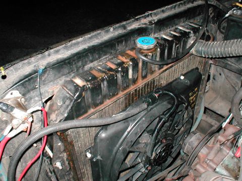 1979 Ford Bronco - Overhead view into an engine bay looking down at a copper/brass radiator with a blue-topped pressure cap, a black electric cooling fan and…